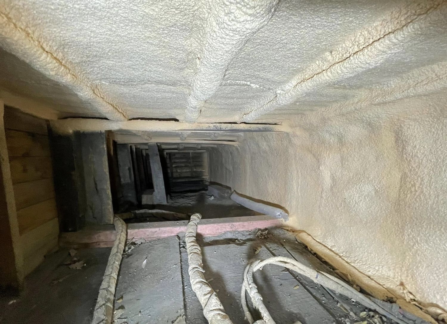 Narrow attic side space with walls and ceiling sealed in spray foam, wiring embedded, old wood floor below