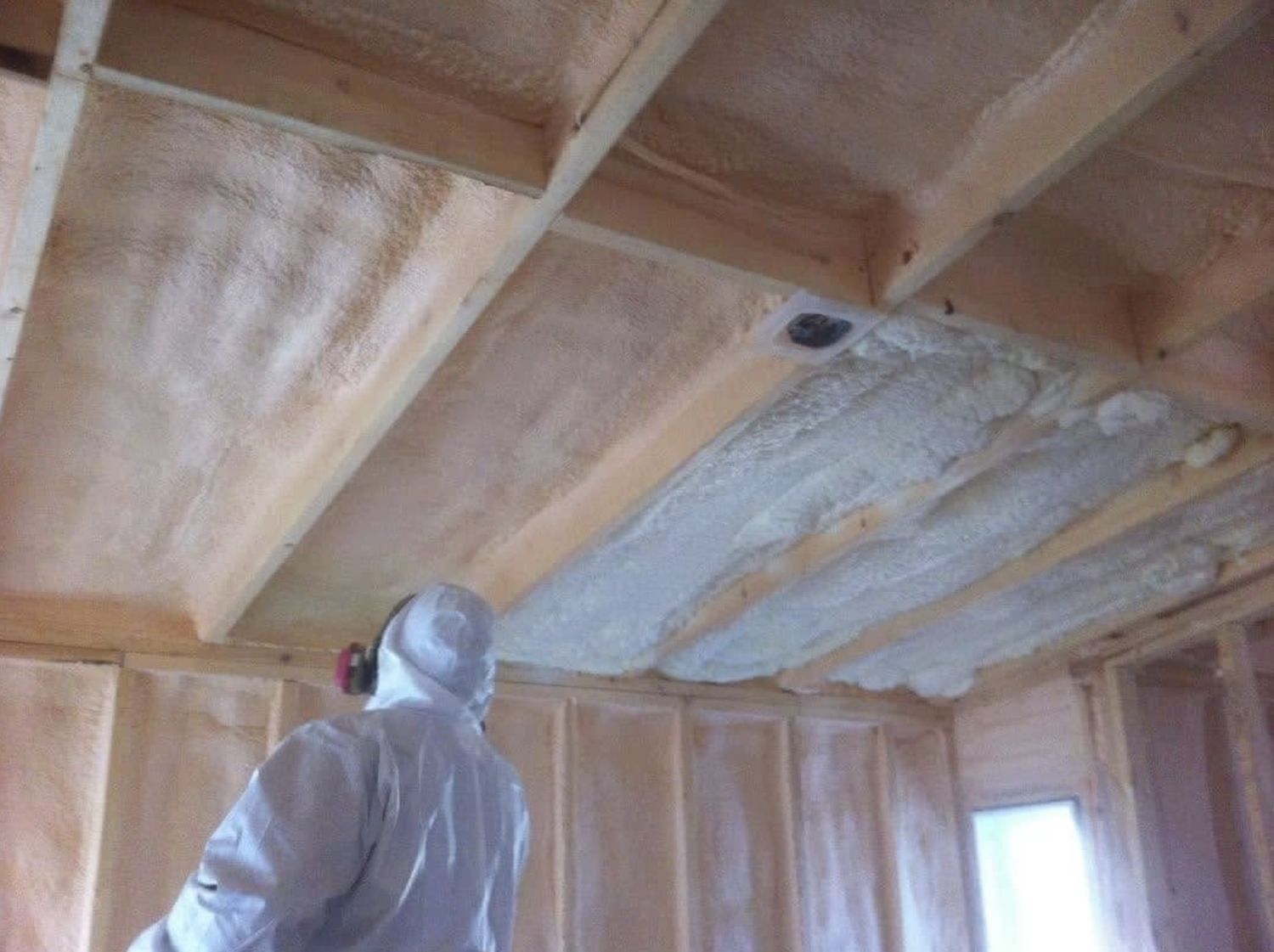 Freshly sprayed foam expanding between ceiling joists beside cured foam during installation