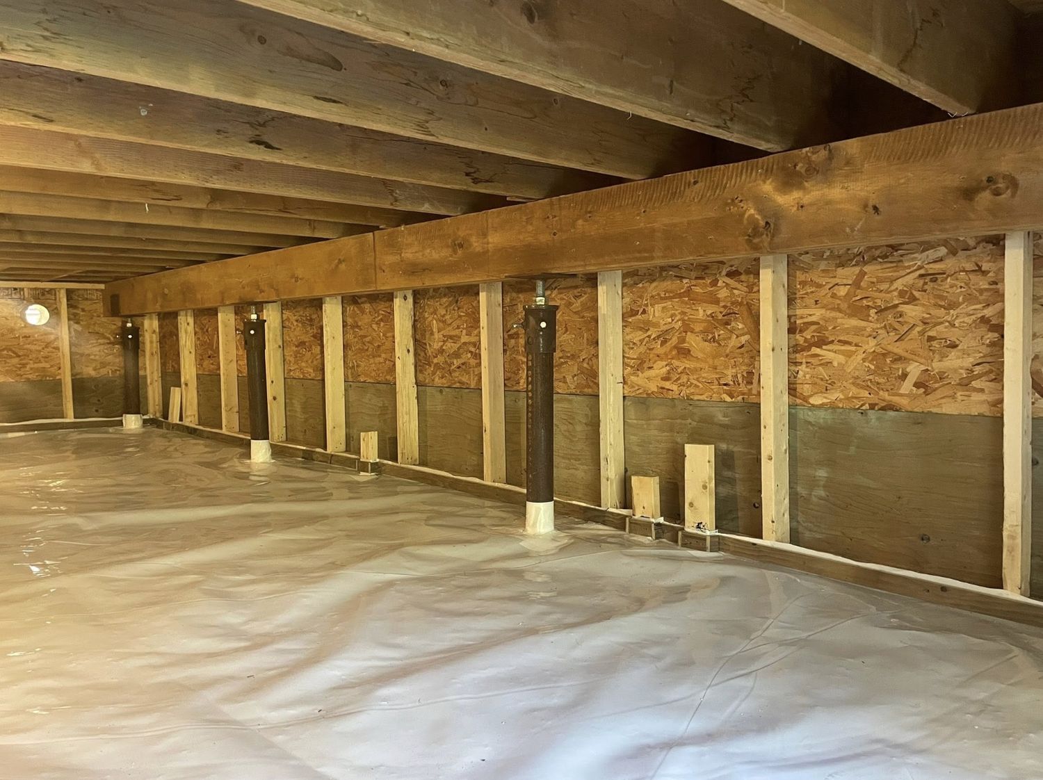 Crawl space prepared for spray foam with bare wood walls, poly ground sheet and wrapped posts