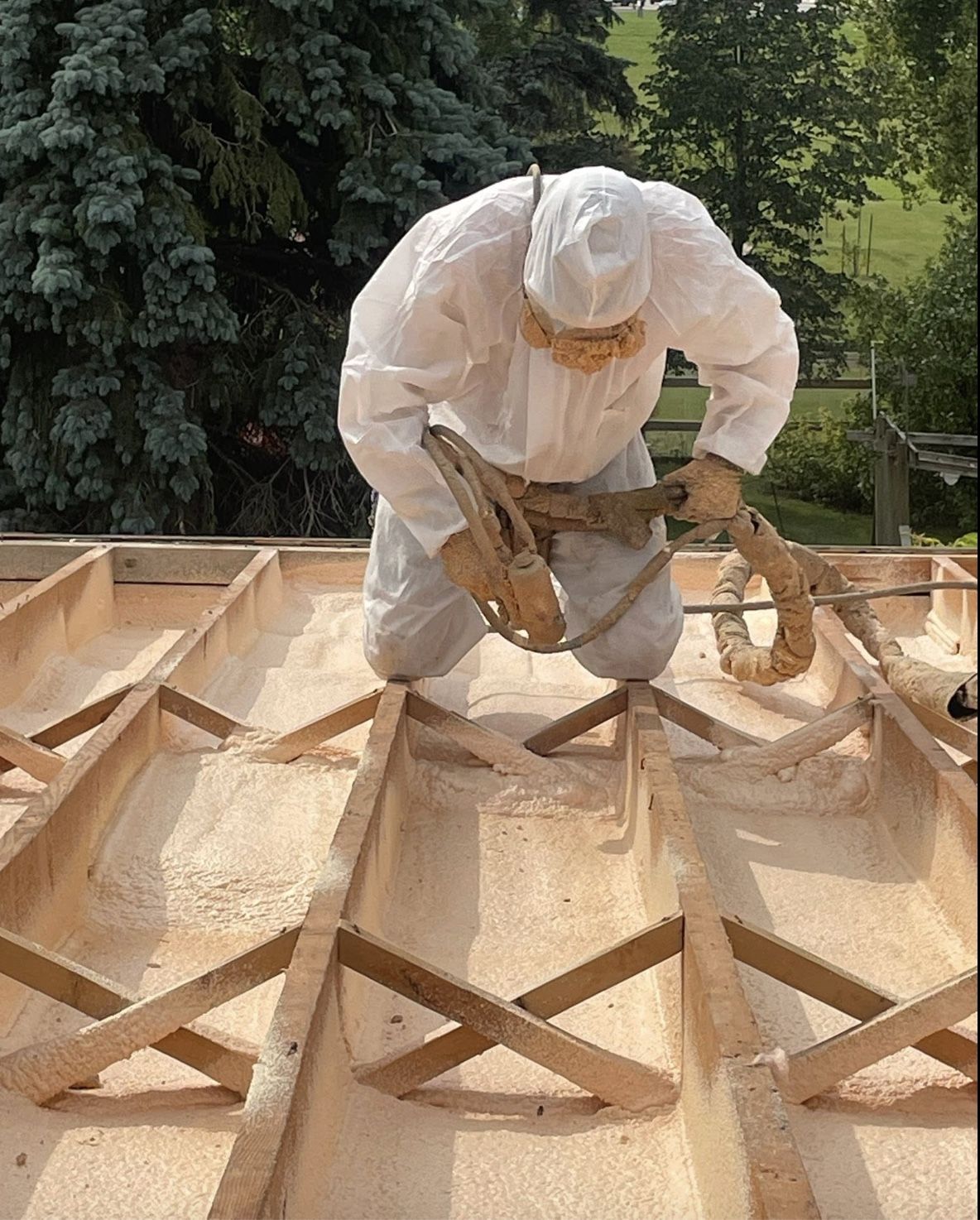 Installer kneeling on an open flat roof spraying foam between the roof joists outdoors