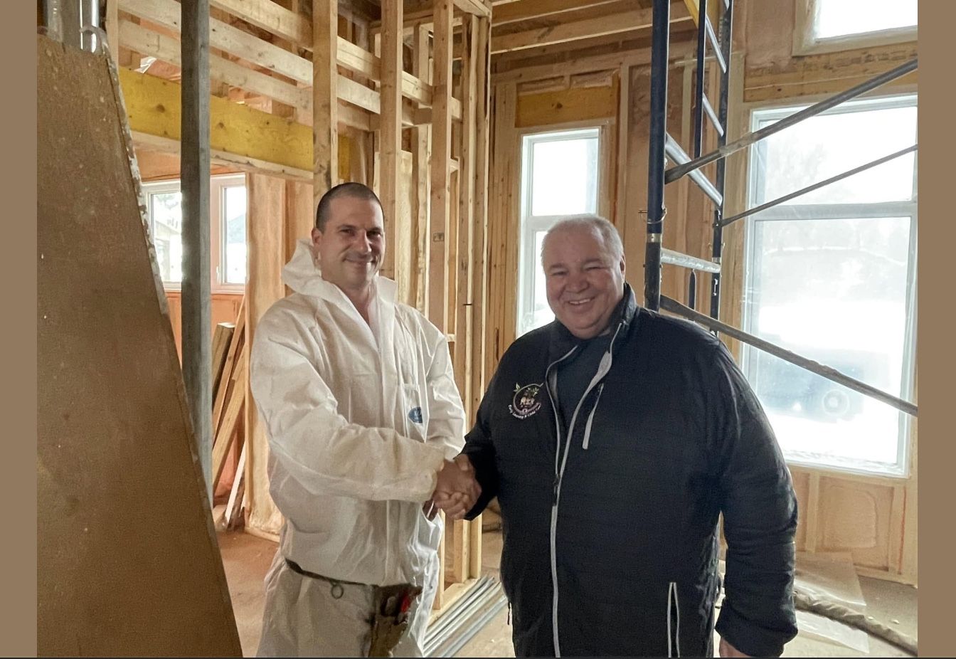 Spray foam installer shaking hands with a client inside a house under renovation