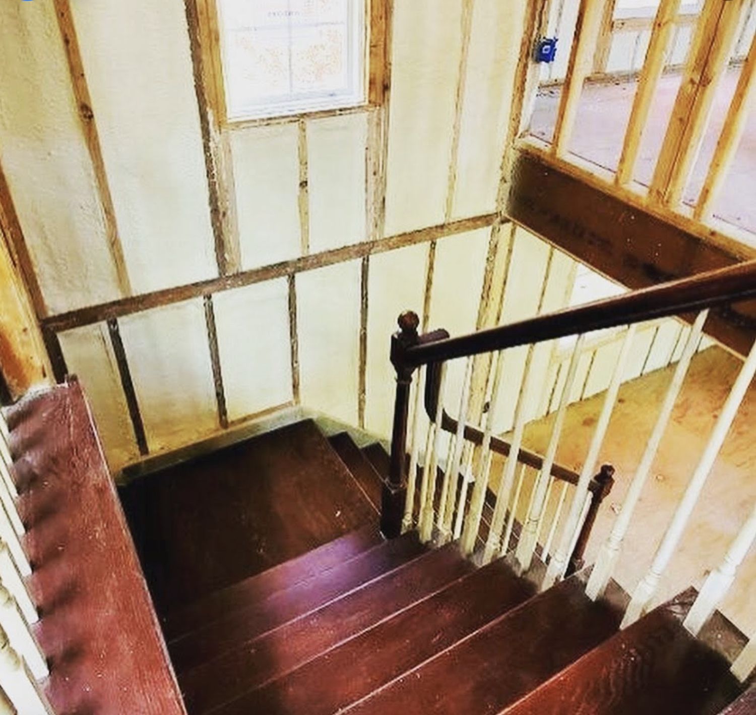 Wood staircase in a home renovation with spray foamed walls between exposed studs