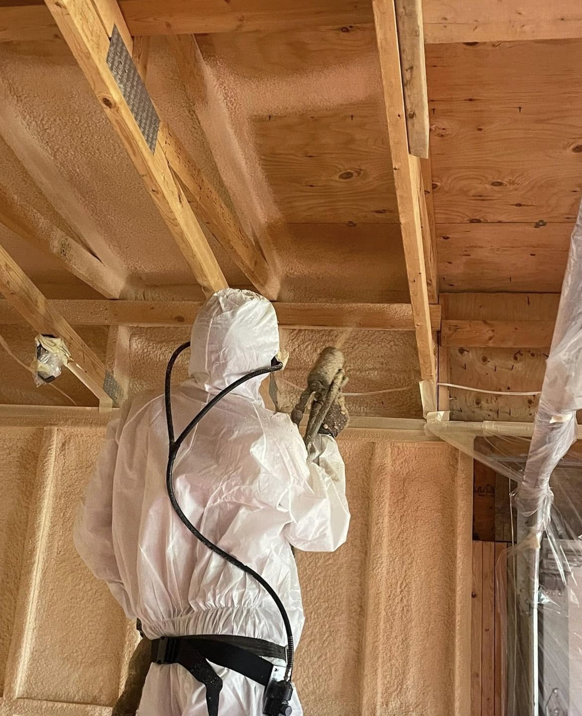 Installer holding a spray gun applying foam where the wall meets the ceiling framing